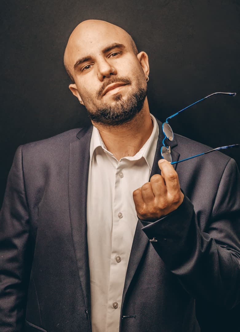 Portrait studio de Damien Benvenuti en costume sombre, lunettes à la main