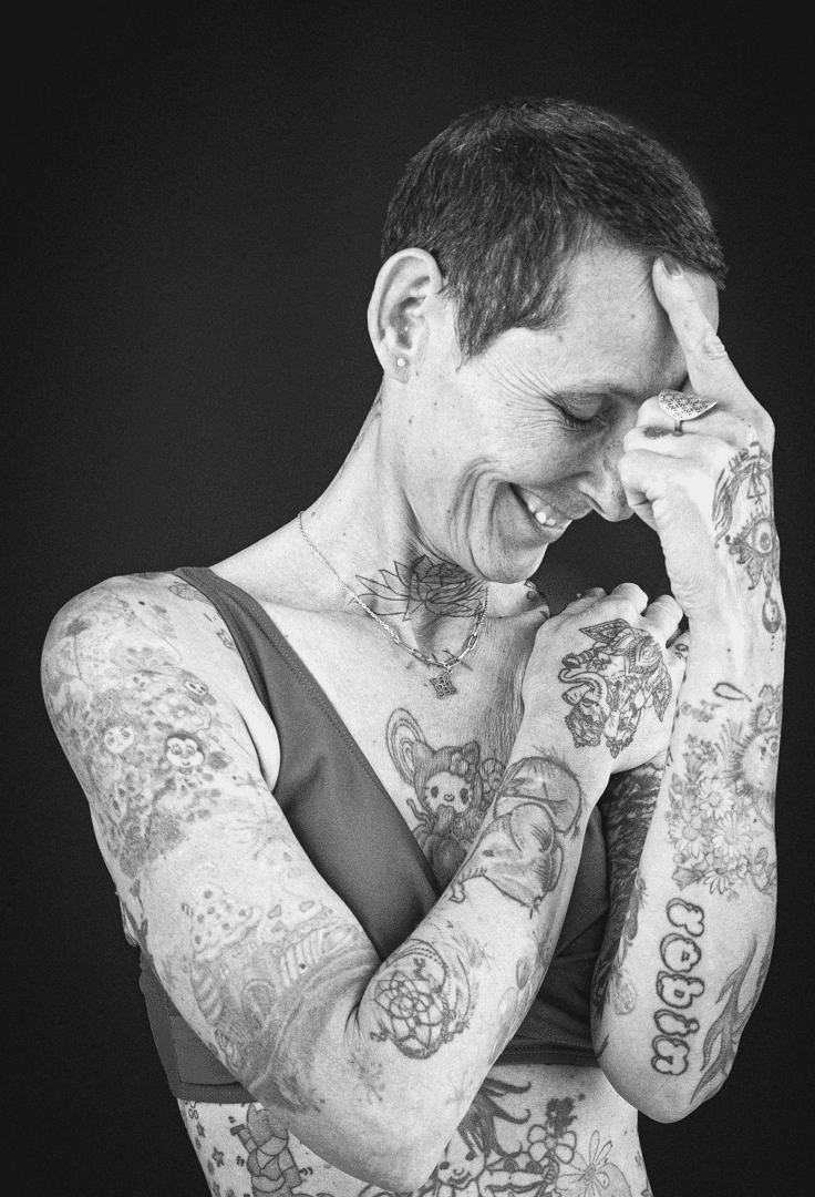 Portrait noir et blanc d'une femme entièrement tatouée, rire spontané, main sur le front