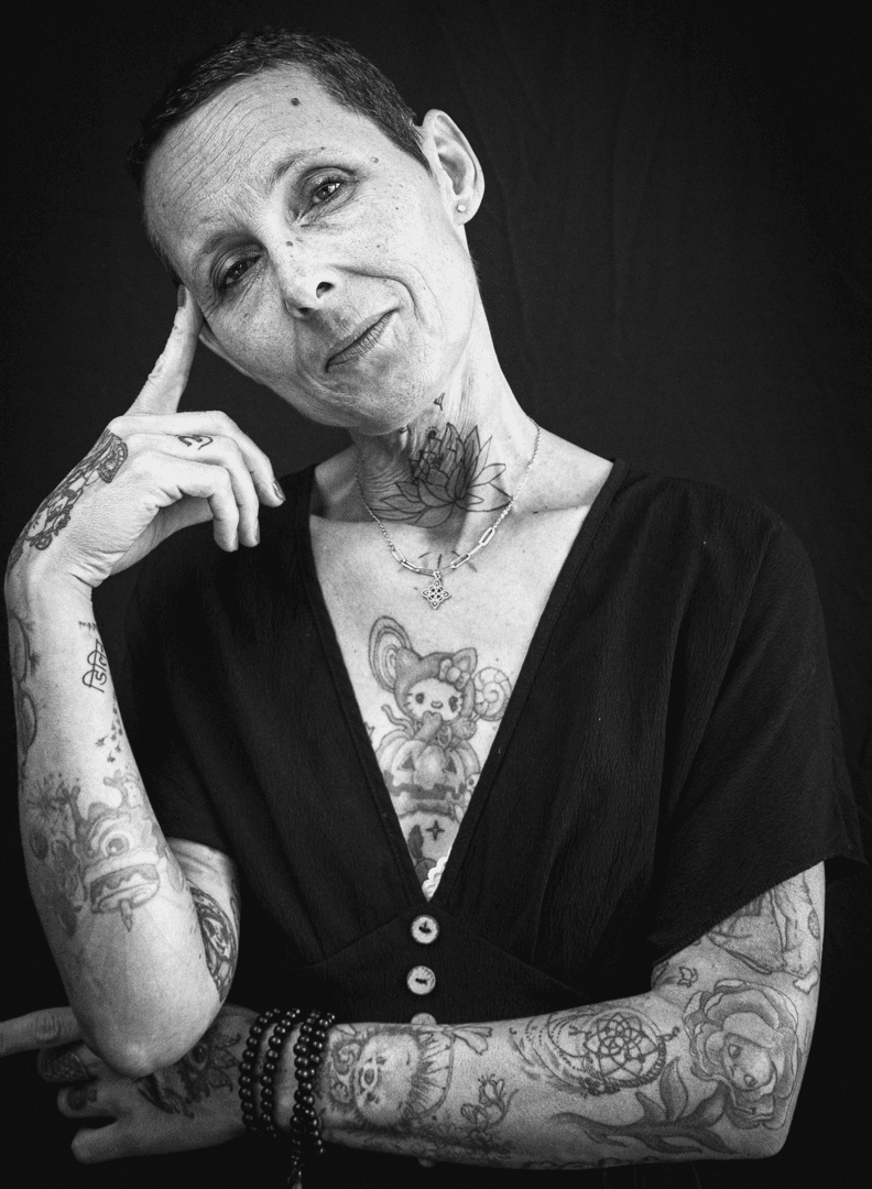 Portrait noir et blanc d'une femme tatouée aux cheveux courts, expression malicieuse