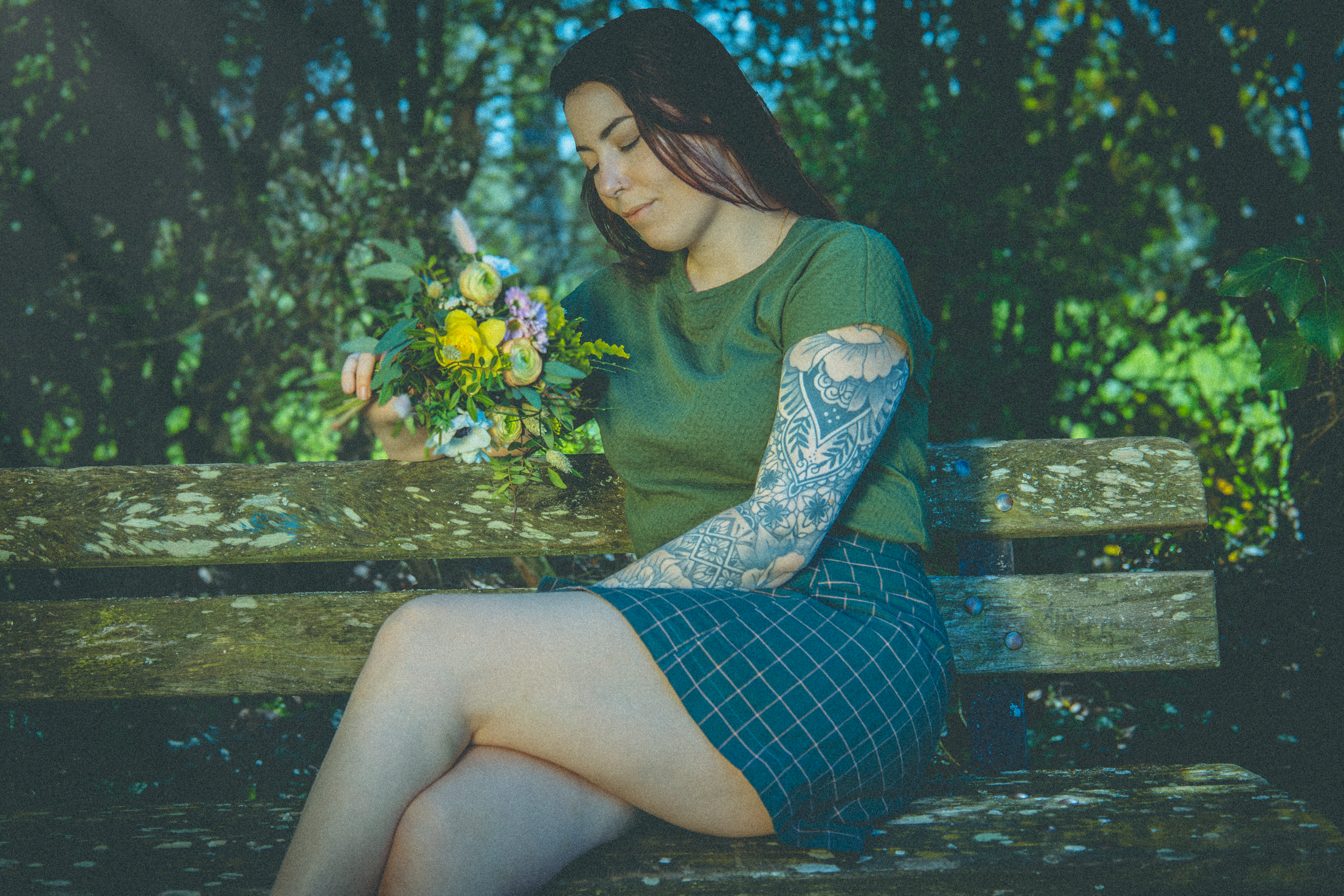 Femme assise sur un banc, manche tatouée fleurie, contemplant un bouquet de fleurs