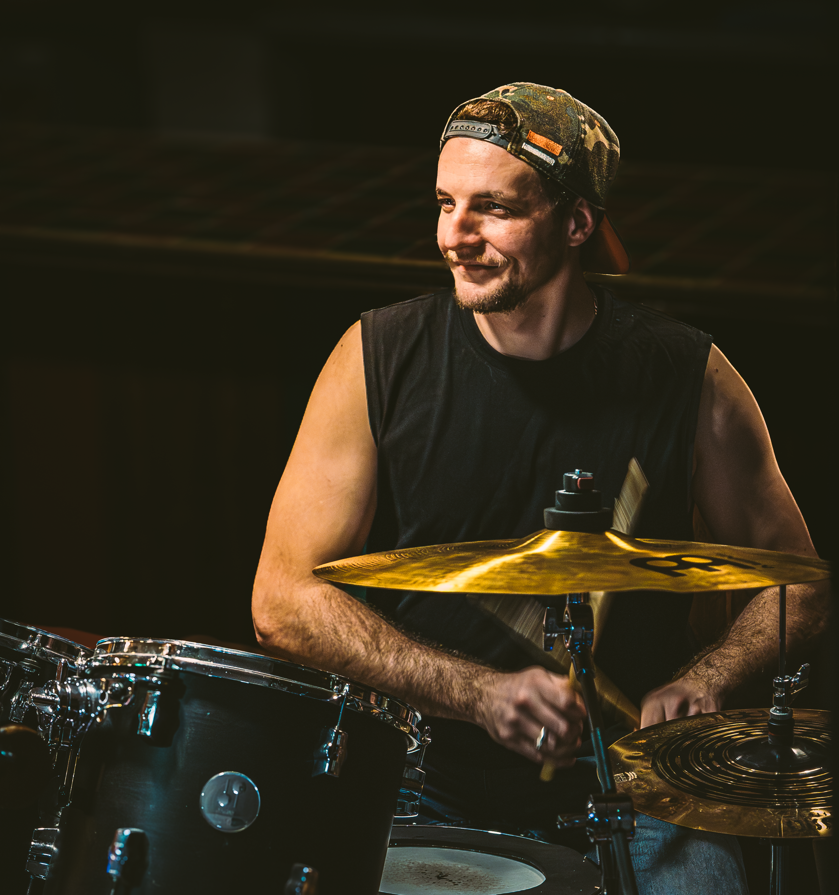 Batteur souriant, casquette à l'envers, cymbale dorée, reportage scène musicale